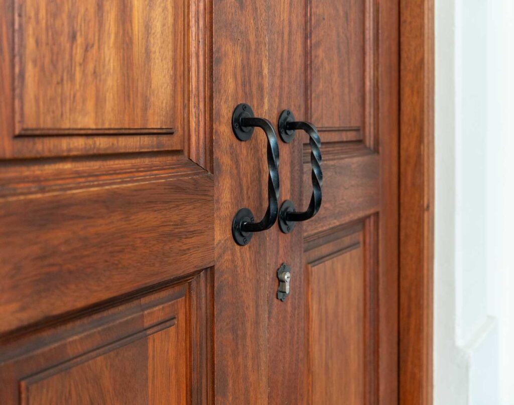 Detalle de jaladeras de hierro forjado sobre puerta de madera tallada